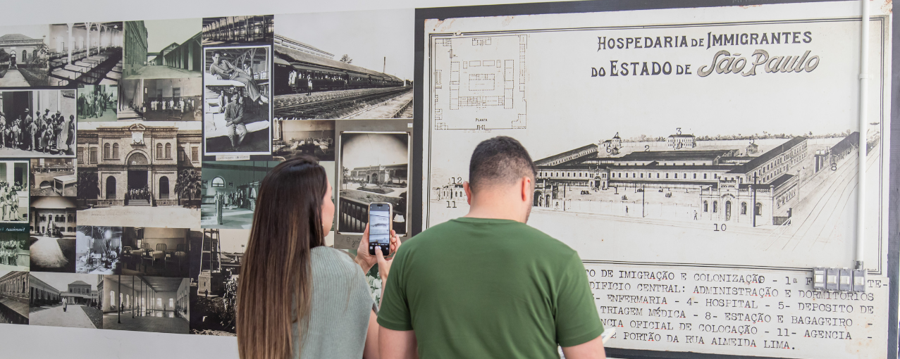 Duas pessoas observando um painel sobre a Hospedaria do Brás.