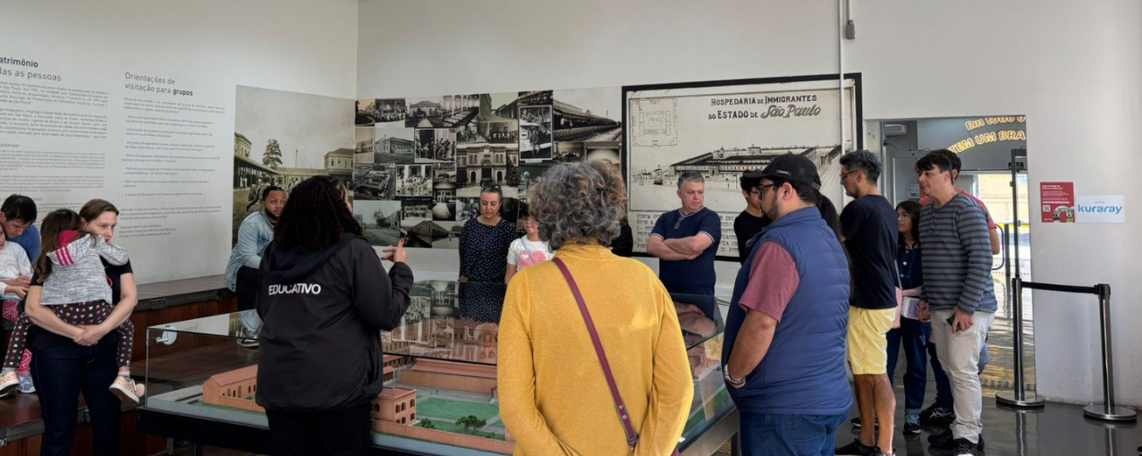 Na imagem, há uma visita sendo mediada por uma das educadoras do Museu da Imigração.